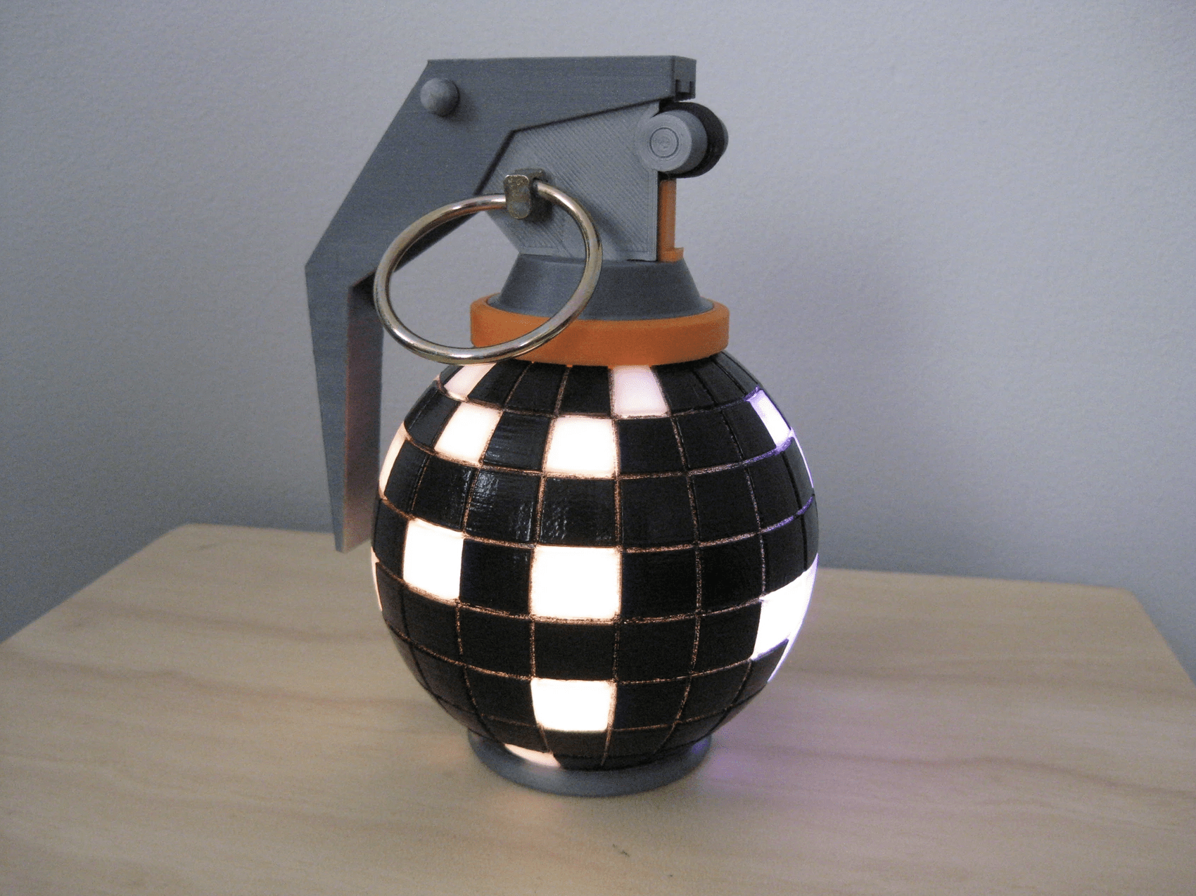 Greencade's photo of its Fortnite Boogie Bomb replica: a black and white checkered ball with an orange collar, a gray lever and a ring pin, on a table